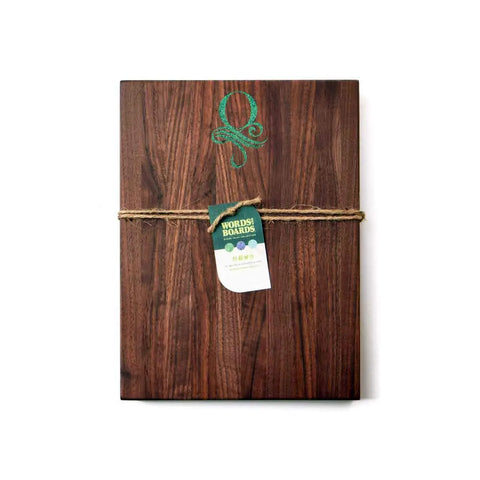 Handcrafted wooden cutting board by Words with Boards, featuring a monogram stone inlay and a green logo. Tied with twine and a Words! Boards tag—perfect for personalized gifts. Made in the USA.