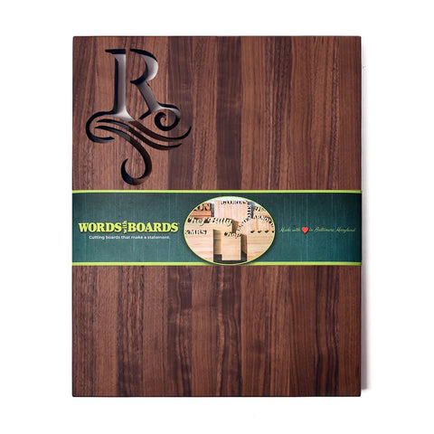 The Handcrafted Wooden Cutting Board – Single Initial Monogram by Words with Boards features a carved initial and flourish, wrapped with a green branded band—a stylish, personalized kitchen accessory and thoughtful gift. Made in the USA.