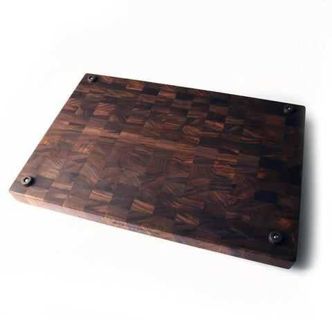 The Handcrafted Wooden Cutting Board by Words with Boards features solid walnut end grain and a checkered design with black feet, making it a chefs favorite. Made in the USA, it looks elegant on any white countertop.