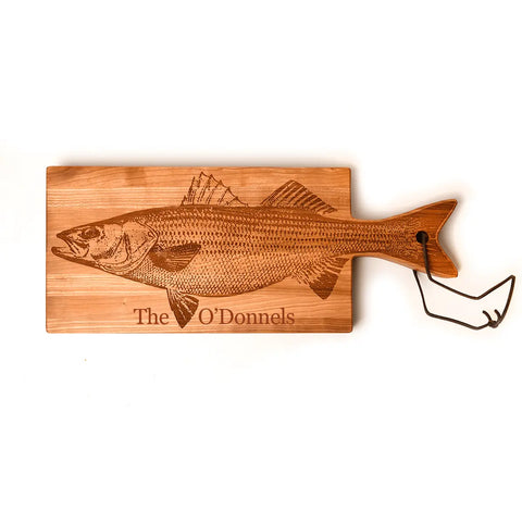 Add charm to your kitchen with the Handcrafted Wooden Fish Shaped Cutting Board by Words with Boards, USA-made and engraved with a detailed fish illustration and “The O’Donnels,” featuring a tail-shaped handle and metal hook.