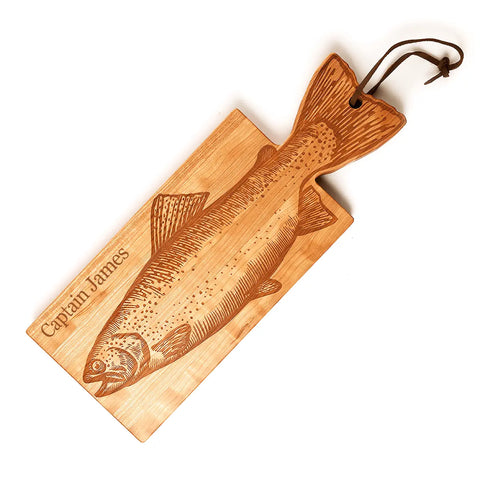 The Handcrafted Wooden Fish Shaped Cutting Board by Words with Boards features a detailed fish illustration and Captain James engraving, plus a tail-shaped handle and leather loop. Made in the USA—ideal as a distinctive serving board or unique kitchen gift.