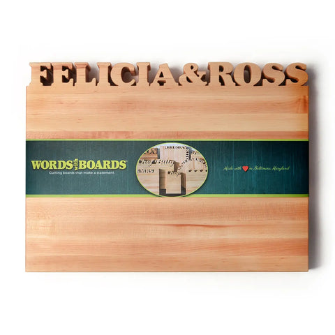 The Handcrafted Wooden Personalized Cutting Board – Large by Words with Boards features “FELICIA & ROSS” cut out along the top and a green band with logo and heart—ideal for kitchen display. Made in the USA from American hardwood.