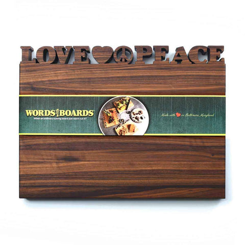 The Handcrafted Wooden Personalized Cutting Board – Large by Words with Boards features LOVE and PEACE cutouts with heart and peace symbols, plus a green branded band. Made in the USA, it’s perfect as a unique kitchen display.