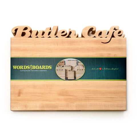 The Handcrafted Wooden Personalized Cutting Board – Large by Words with Boards, made in the USA, features “Butler Cafe” cut out at the top and a green Words with Boards label—perfect for display in any kitchen.