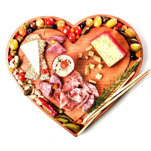 The Handcrafted & Heart Shaped Wooden Cheese Board by Words with Boards beautifully serves an assortment of cheeses, cured meats, nuts, olives, cherry tomatoes, pickles, and breadsticks—garnished with rosemary and spice.