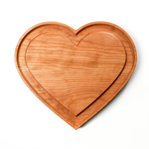The Handcrafted & Heart Shaped Wooden Cheese Board by Words with Boards is a cherry wood charcuterie board with a groove outlining the heart—perfect as a serving tray, shown on a white background. Made in the USA.