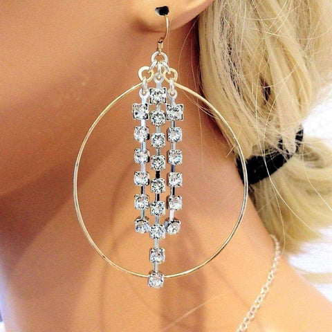 A woman with blonde hair in a black hair tie wears Alexa Martha Designs’ Golden Oval Hoop Crystal Chain Earrings, featuring dangling rows of sparkling crystals.