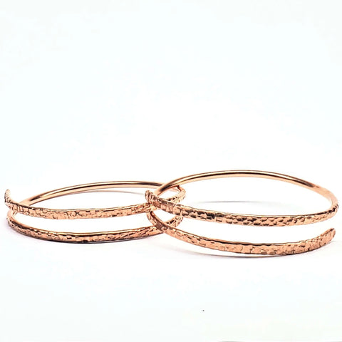 The Alexa Martha Designs 2 Piece Handmade Interlocking Full Overlap Copper Bangle Set features two textured copper bangles with a shiny, modern finish, elegantly overlapping on a white background.