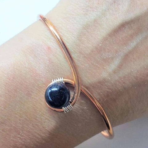 A hand wearing the Alexa Martha Designs Handmade Copper Silver Ribbon Child Abuse Awareness Teardrop Bangle, featuring a minimalist handcrafted design.