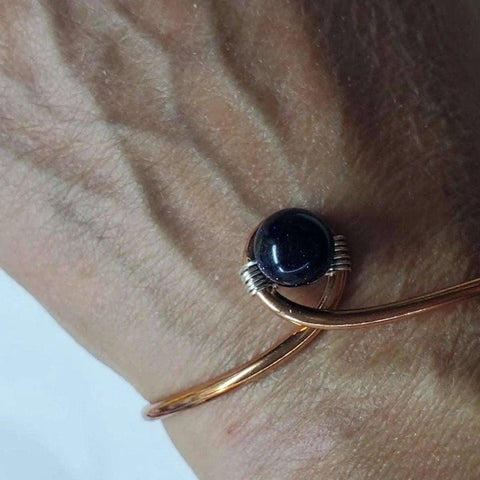 A close-up shows a hand wearing the Alexa Martha Designs Handmade Copper Silver Ribbon Child Abuse Awareness Teardrop Bangle, which gently curves around the wrist with visible veins on the skin.