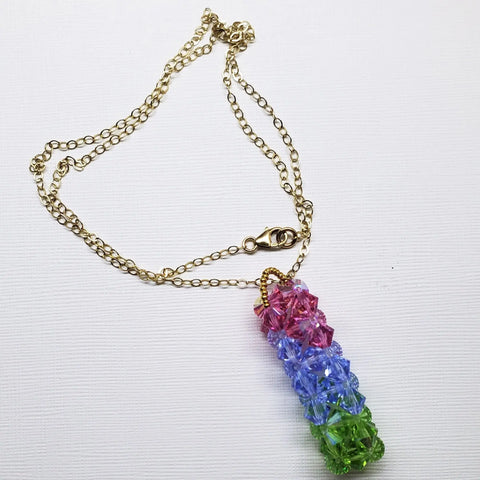 The Super Sparkly Crystal Pillar Pendant in Green Blue and Rose by Alexa Martha Designs features stacked faceted beads in a gold chain necklace, sparkling with Swarovski crystals and shown on a white background.