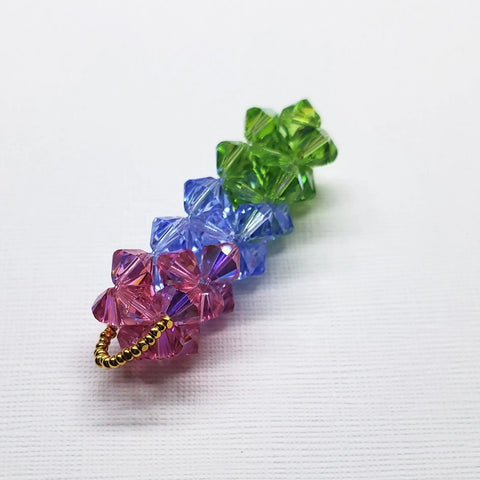 The Super Sparkly Crystal Pillar Pendant in Green Blue and Rose by Alexa Martha Designs features stacked crystal flower shapes with gold beads, shown on a white textured background. Optional necklace available.