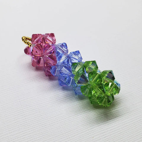 The Super Sparkly Crystal Pillar Pendant by Alexa Martha Designs features green, blue, and rose crystals in a floral gradient, shown on a white textured background. Optional necklace available.
