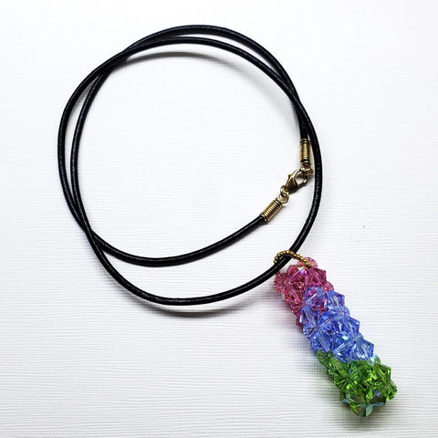 The Super Sparkly Crystal Pillar Pendant in Green, Blue, and Rose by Alexa Martha Designs is shown on a black cord necklace against a white background.