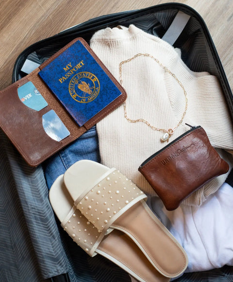 An open suitcase with a cream sweater, blue jeans, white shirt, bead-embellished sandals, gold necklace, brown leather pouch, and the Urban Southern Passport Wallet—your perfect travel companion.