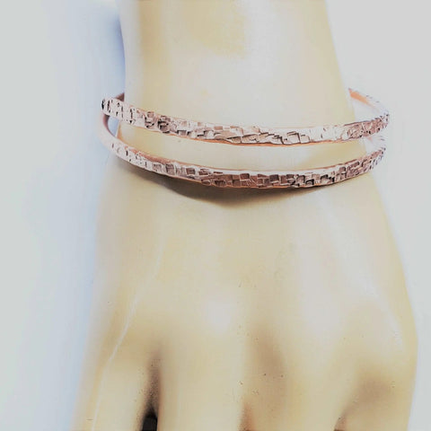 A mannequin hand displays two textured Full Overlap Copper Bangles by Alexa Martha Designs in a rose gold tone against a light background.