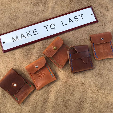 Five Sully + Proper Supply Coin Pouches with colored stitching are displayed on a tan leather surface below a MAKE TO LAST sign—a minimalist leather accessory, handmade in the USA.