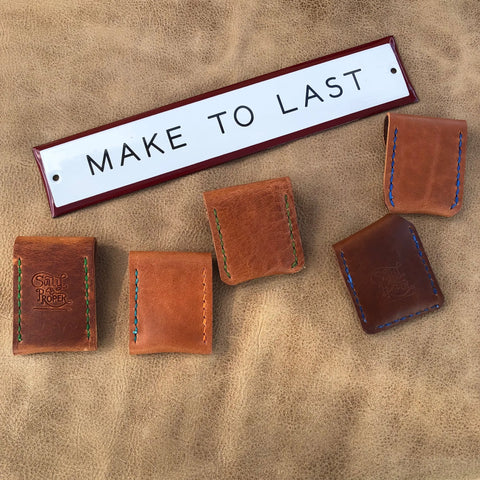 Five brown Coin Pouches by Sully + Proper Supply with colorful stitching are arranged on leather below a MAKE TO LAST sign. Two pouches show the brands logo, highlighting these minimalist leather accessories handmade in the USA.