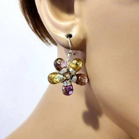 A close-up of a light-skinned ear wearing Alexa Martha Designs’ Purple and Yellow Flower Sterling Silver Earrings, accented with purple and gold Czech glass beads.