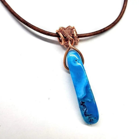 The Wire Wrapped Pointed Turquoise Agate Leather Necklace for Him and Her by Alexa Martha Designs features a turquoise agate pendant wrapped in copper on a brown leather cord, shown against a white background.