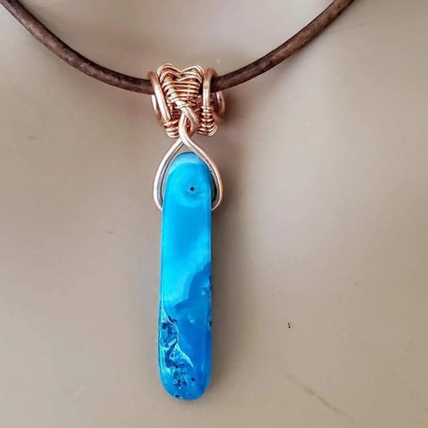 The Wire Wrapped Pointed Turquoise Agate Leather Necklace for Him and Her by Alexa Martha Designs features a marbled blue stone wrapped in copper on a brown leather cord, blending natural style and unique craftsmanship.
