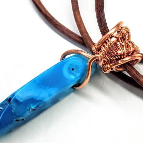 The Wire Wrapped Pointed Turquoise Agate Leather Necklace for Him and Her by Alexa Martha Designs features a blue stone pendant wrapped in copper wire on a brown leather cord—ideal as handmade jewelry.