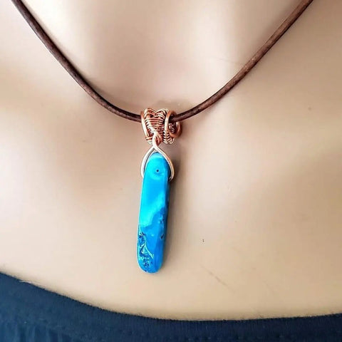 A close-up of the Alexa Martha Designs Wire Wrapped Pointed Turquoise Agate Leather Necklace for Him and Her, featuring a blue marbled stone pendant on a brown cord—an eye-catching handmade unisex accessory.