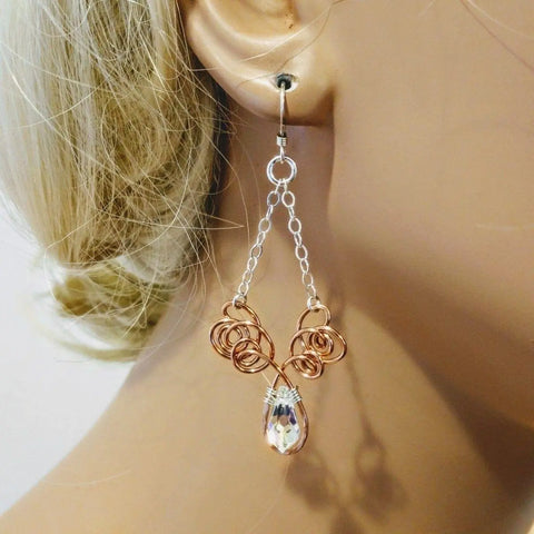A close-up of a mannequin with blonde hair pulled back modeling Alexa Martha Designs Wire Sculpted Crystal Drop Chandelier Angel Wing Earrings—handcrafted with copper, silver chains, rose gold swirls, and a teardrop crystal pendant.