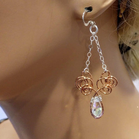 A close-up of a mannequin wearing Alexa Martha Designs Wire Sculpted Crystal Drop Chandelier Angel Wing Earrings—handcrafted with copper, silver chain, wire swirls, and a faceted teardrop crystal.