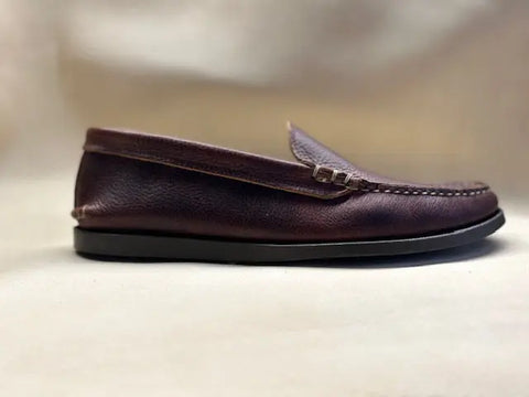 The BBH Loafer, shown in profile against a soft, neutral background, features brown handsewn pebble grain leather with visible stitching and a black sole.