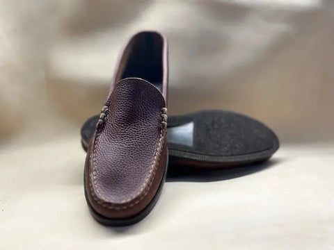 A pair of BBH Loafers in brown pebble grain leather is shown on a light surface, with one shoe behind the other to highlight the textured upper and black sole—a tribute to classic American shoemaking.