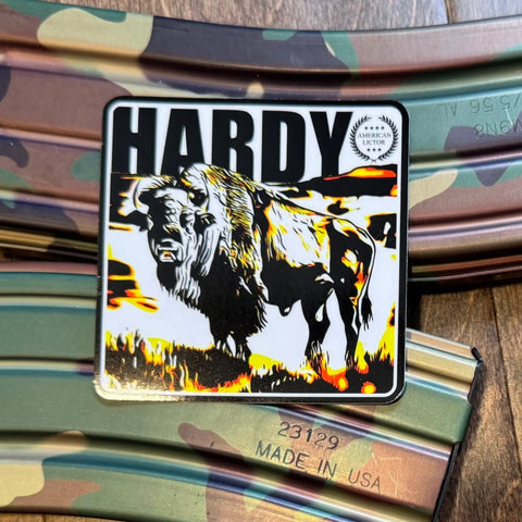 The American Lictor Sticker: Bison - Hardy is a 3 x 3 square with bold black, yellow, and orange bison art over camouflage metal and MADE IN USA label—a striking tribute to the free and powerful American icon.