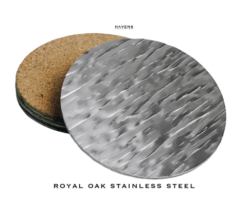 A round, textured stainless steel drink coaster by Havens Luxury Metals is stacked in front of a cork-backed coaster on a white background. Each features heavy-duty design and is labeled “Drink Coasters - Stainless Steel.”.