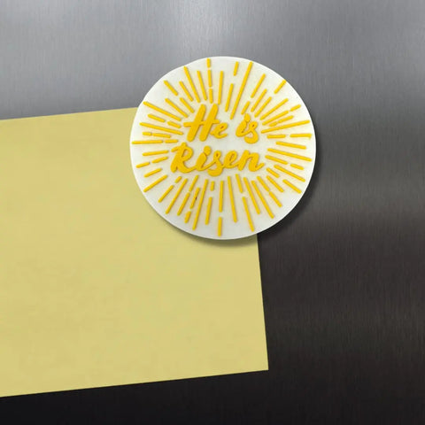 The Chatelet Manufacturing He Is Risen Easter Decorative Fridge Magnet, in yellow and white, holds a blank yellow note on a stainless steel fridge—an uplifting Easter decoration that celebrates Jesus’s resurrection. Made in the USA.