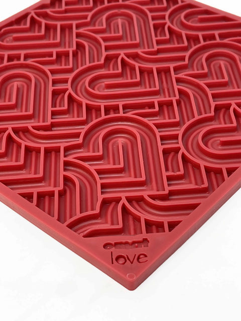 The SodaPup Heart Design Love EMat Lick Mat is a red silicone dog enrichment toy with a raised geometric heart pattern and love embossed in the corner, shown on a white surface.