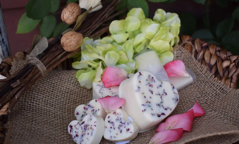 Bathsheba Body Works Moisture Bar - Love Me features heart-shaped artisan white soaps for mature skin, displayed on burlap with pink rose petals, green hydrangea blooms, and rustic twigs in a woven basket.