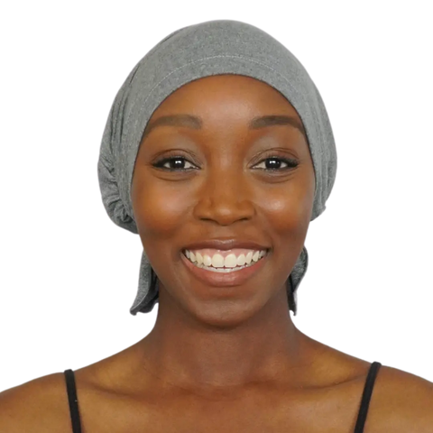 A smiling woman wears the Chemo Beanies® Patricia scarf in grey with a black strap top, looking directly at the camera against a plain background.