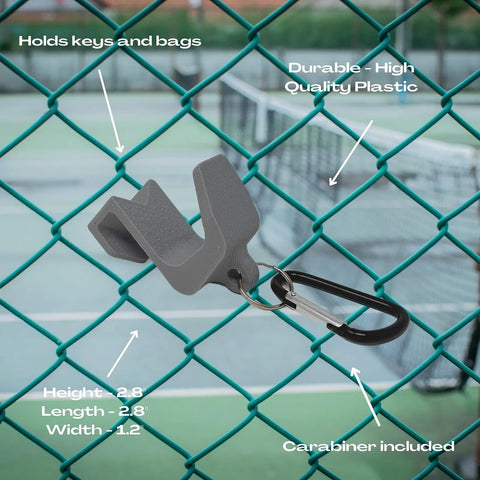 A Chatelet Manufacturing Carabiner Fence Holder in gray plastic hangs on a green chain-link fence near a tennis court. Features noted in white text: holds keys/bags, durable material, carabiner attachment, product dimensions included.