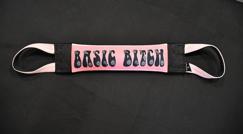 The Basic Bitch Fire Hose Training Tug by Bulletproof Pet Products Inc features a pink fabric strap with black ends and handles, bold “BASIC BITCH” text, and a durable design—an ideal dog tug toy for tough play.