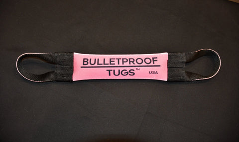 A pink and black Basic Bitch Fire Hose Training Tug by Bulletproof Pet Products Inc, featuring two black loop handles, lies on a black surface.