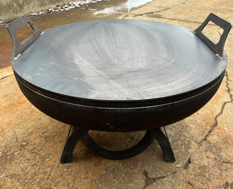 The Ohio Flame Flat Fire Pit Lid (Made in USA) is a large, round, black lid with two square handles on opposite sides, designed to sit securely on your fire pit and rests steadily on flat surfaces.