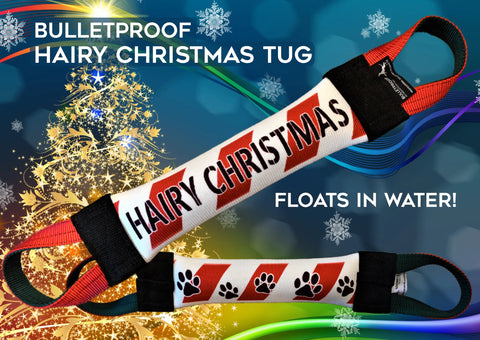 A festive, durable red and white Bulletproof Pet Products Hairy Christmas Fire Hose Training Tug for dogs, with black handles and paw prints. Features a Christmas tree background. Floats in water! Holiday Series.