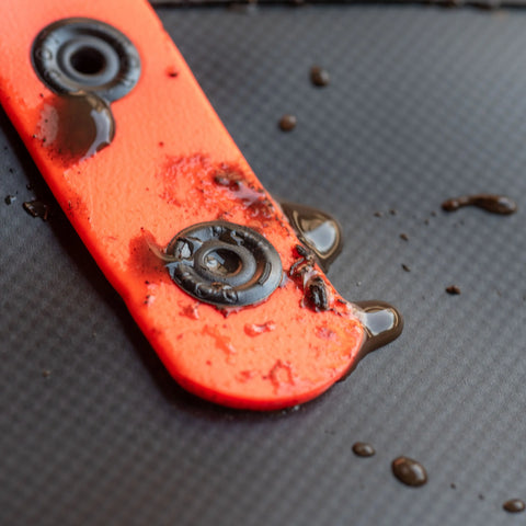 A close-up of the eqpd DirtBag, an orange rugged tote with metal rivets splattered with wet brown mud, rests on a dark textured surface—ideal gear for trail builders.