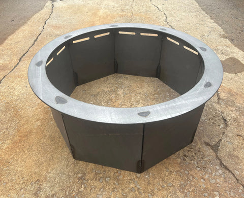 An Ohio Flame Heavy Gauge Fire Ring - Round (Made in USA) rests on a cracked concrete surface, featuring rectangular vents near the top of each panel for improved airflow.