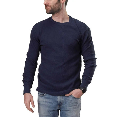 A bearded man wearing a dark blue Spiritex | Sustainable Apparel Long Sleeve Crewneck Heavy Thermal shirt and light blue jeans stands against a white background, looking to his left with one hand in his pocket.