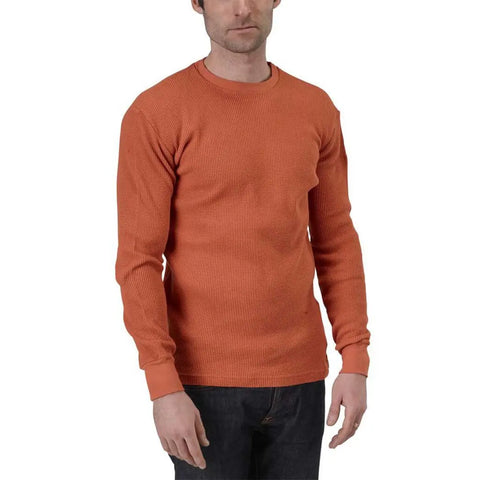 A man wearing a Spiritex Long Sleeve Crewneck Heavy Thermal in orange and dark jeans stands against a plain white background.