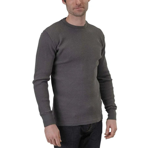 A man stands slightly turned, wearing a Spiritex | Sustainable Apparel Long Sleeve Crewneck Heavy Thermal shirt in grey with dark jeans. His face is partially visible against a plain white background.