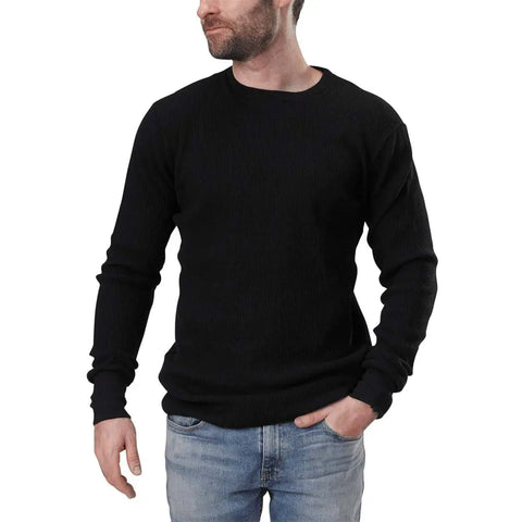 A man with a short beard wears a black Spiritex Long Sleeve Crewneck Heavy Thermal sweater and light blue jeans, standing with one hand in his pocket and looking to the side against a plain white background.