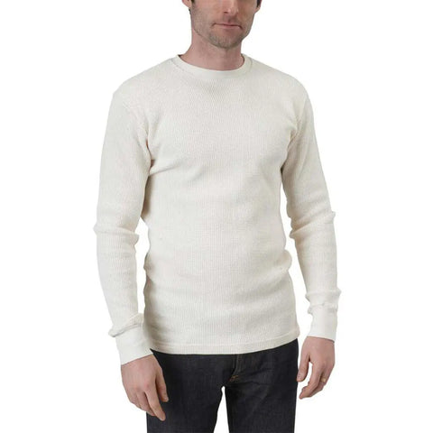 A man stands facing forward against a plain white background, wearing the Spiritex | Sustainable Apparel Long Sleeve Crewneck Heavy Thermal in off-white and dark jeans, with his arms relaxed by his sides.