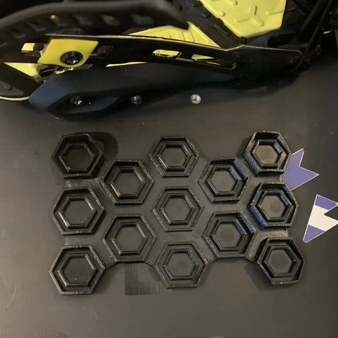 The Chatelet Manufacturing Snowboard Stomp Pad features a black and yellow hexagon pattern, offering specialized grip and weatherproof adhesion for your snowboard.